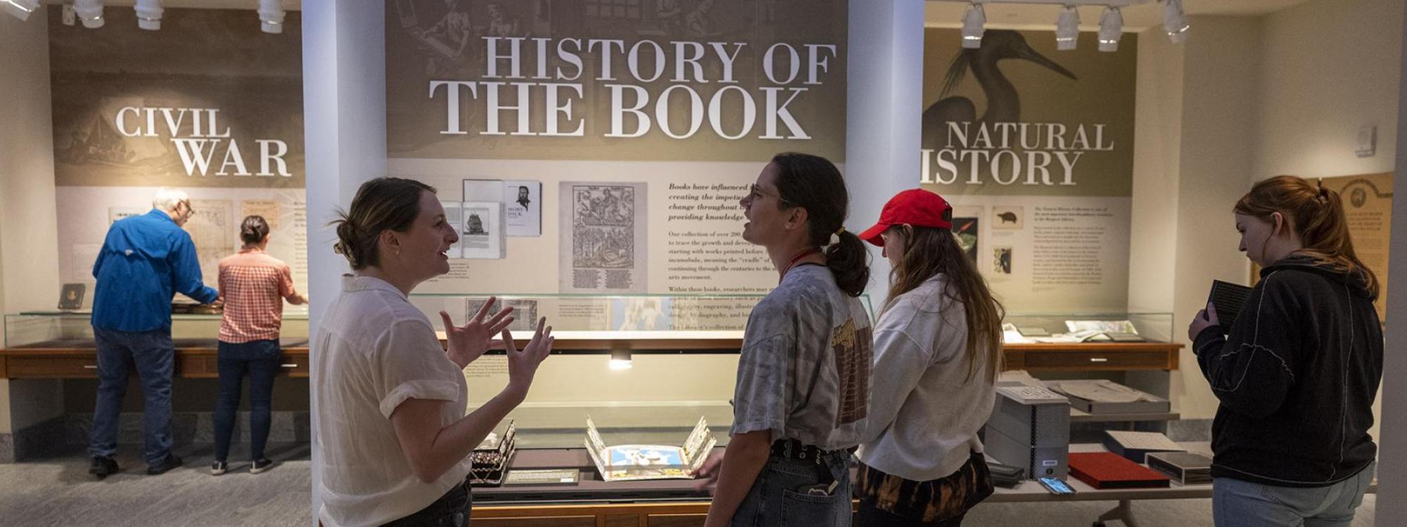 Students standing in front of an exhibit called history of the book while engaged in active discussion.