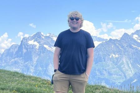 Charles Dew in Switzerland, photographed in front of the scenic Swiss Alps on a mountainside.