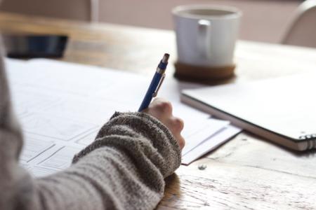 photo of person with pen in hand and coffee cup at desk