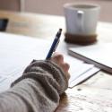 photo of person with pen in hand and coffee cup at desk